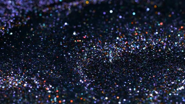 Shimmering multicolored glitter particles on a dark textured surface