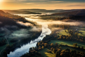 Fototapeta premium Aerial view showing river winding through misty valley, hills, and autumn forest during sunrise