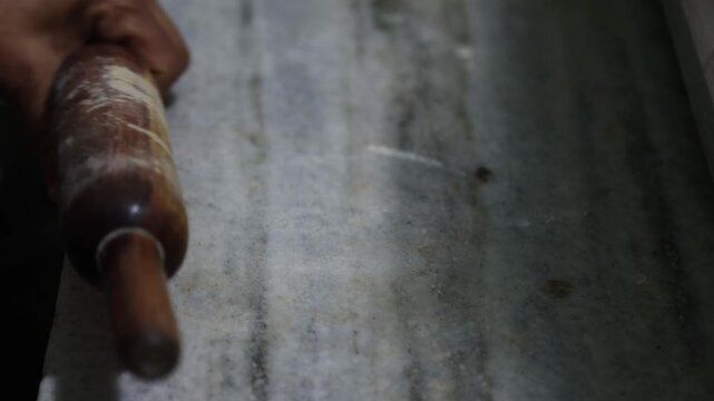 Rolling coarse grain millet dough on a traditional stone slab for chapati making, using nutrient-dense grains like jowar, bajra, and ragi, showing healthy food preparation, manual technique.