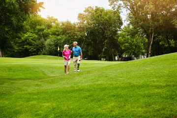 Fototapeta premium Senior couple, happy and walk at golf course with chat, laugh and bonding on vacation in summer. People, conversation and golfer with funny story, recreation or game on holiday at country club