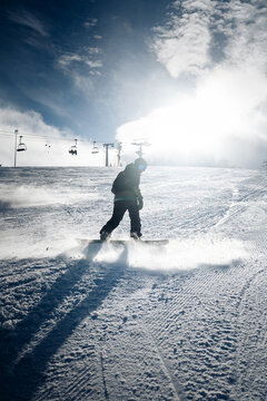 Snowboarder carving fast downhill on sunny ski slope with chairlifts