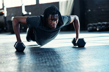 Fototapeta premium Black man, push up and dumbbells for fitness at gym with exercise, muscle development or power on floor. African person, bodybuilder and training equipment for challenge, strong or workout at club