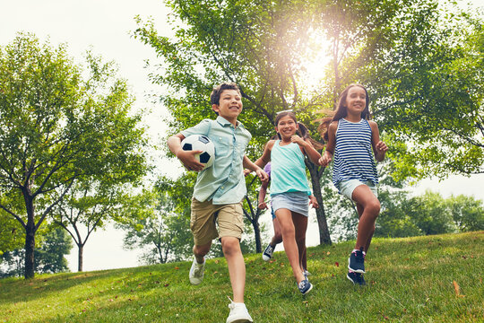 Friends, children and happy for running at park with football, outdoor and bonding on summer vacation. Kids, group and excited at playground with soccer ball, smile or low angle with games in nature