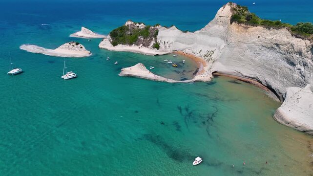 Aerial Drone Video of Cape Drastis Peroulades in North Corfu Greece Featuring Dramatic White Cliffs and Secluded Coves with Anchored Boats in Crystal Clear Blue Water