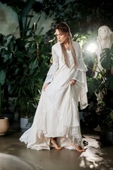 Woman in flowing white dress with bell sleeves posing among lush green plants and statue
