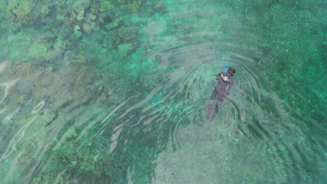 Aerial view of a person snorkeling in clear turquoise ocean water near coral ree
