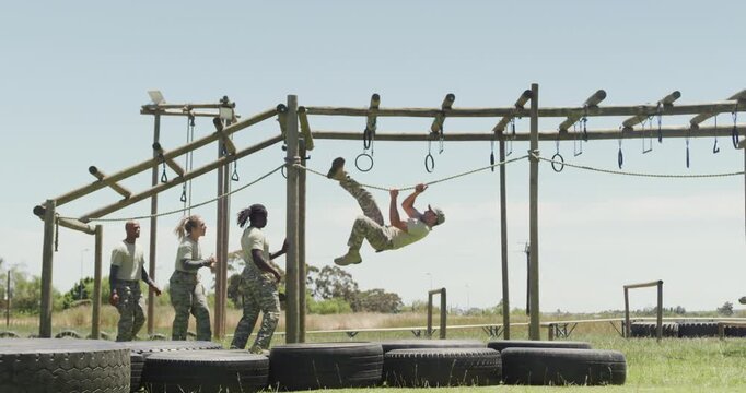 Fit diverse group of soldiers using hanging rope and rings on army obstacle course in the sun