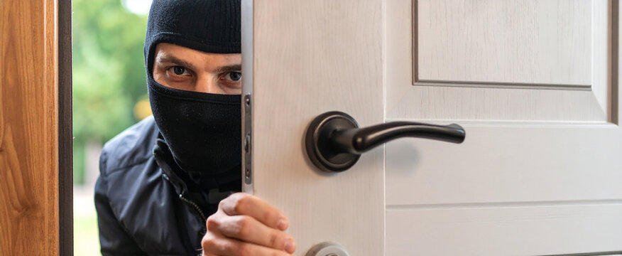 Ladron encapuchado forzando la puerta de entrada de una vivienda sin alarma antirrobo, concepto de robo, ocupaci&oacute;n, allanamiento y vulnerabilidad e inseguridad del hogar 