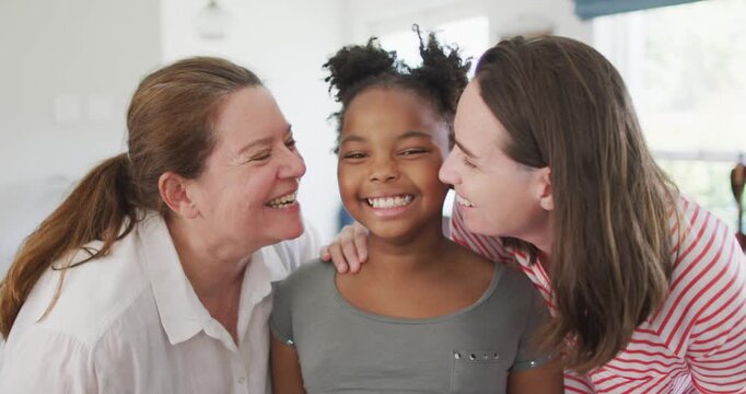 Happy caucasian lesbian couple and their african american daughter embracing with smiles