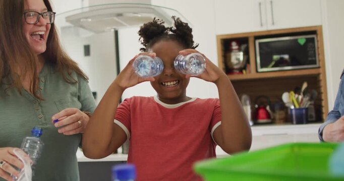 Happy caucasian lesbian couple and their african american daughter sorting waste in kitchen
