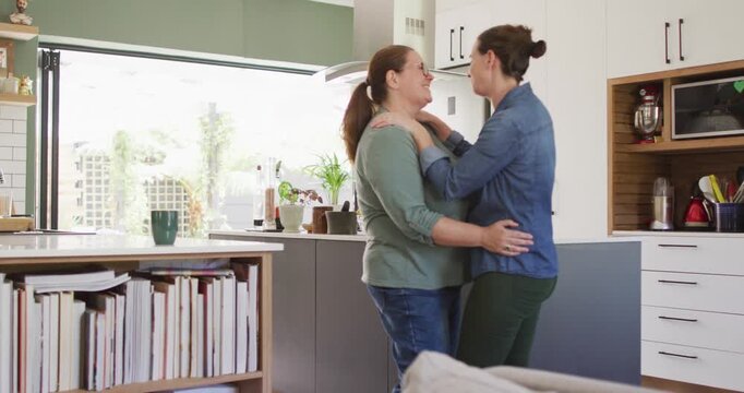 Caucasian lesbian couple smiling and dancing in kitchen