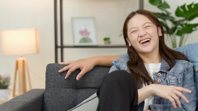 Young Asian woman laughing on cozy living room sofa
