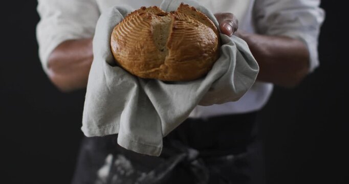 Video of cook holding loaf of bread on black background