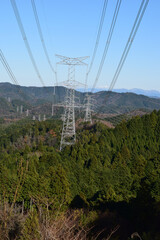 山並みを越えて連なる送電鉄塔と高圧電線の風景