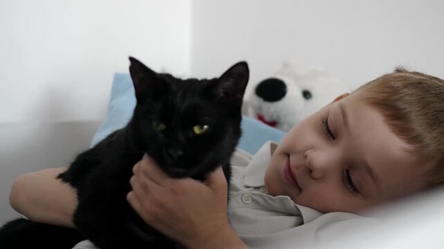 Happy little boy relaxing at home while cuddling his black cat. Warm, cozy family moment showing love, friendship and trust between child and pet.