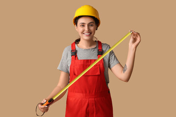 Young female construction worker with measuring tape on beige background. Woman in male profession...