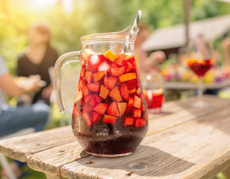 A refreshing glass pitcher filled with fruit infused drink on a wooden table outdoors in a garden setting viewed from the side
