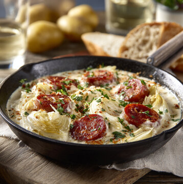d&rsquo;un plat chaud de fonduta di indivia con salsiccia affumicate, servi dans une po&ecirc;le en fonte noire ou un plat rustique en c&eacute;ramique, plac&eacute; au centre d&rsquo;une table en bois.