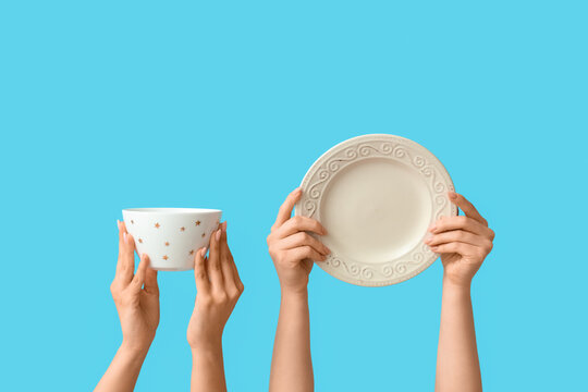 Hands holding empty plate and bowl on blue background