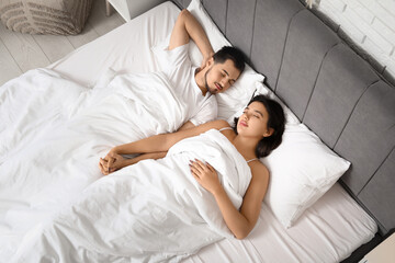 Asleep young couple holding hands in bed at home, top view