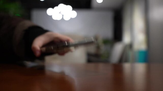 A hand grabbing and picking up a mobile phone on restaurant table