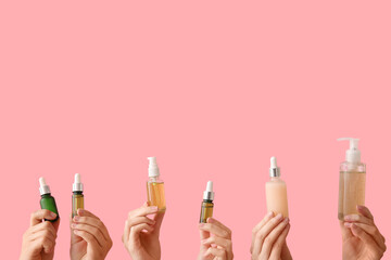 Female hands with different bottles of cosmetic products on pink background