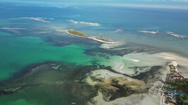 Wide natural seascape aerial highlighting palm-covered island, white sand beaches, and crystal clear water.