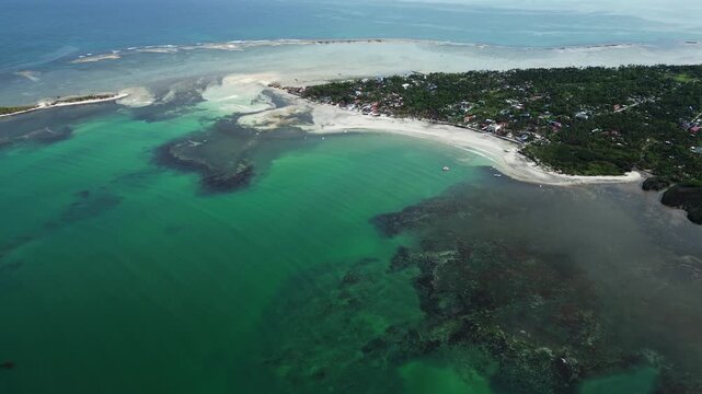 Diagonal aerial angle showing palm-lined island shore, white sand, and crystal clear water at Tondol.