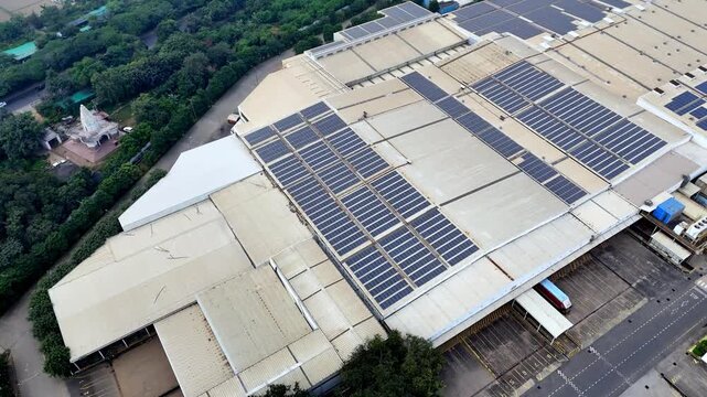 Drone footage over expansive factory roofs fitted with solar panels, highlighting sustainable energy efforts in Greater Noida while atmospheric smog subtly reveals ongoing urban and industrial area.