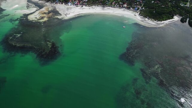Low altitude aerial pass revealing palm trees, bright white sand, and clear island water at Tondol.