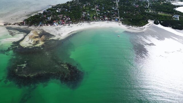 Wide aerial composition with clear water in the foreground framing the palm-covered island and white sand.