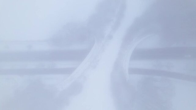 Aerial top down descending through mist revealing Dutch snow landscape with environment nature reserve infrastructure ecoduct in hazy winter conditions