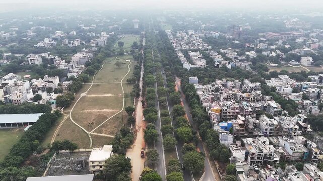 Aerial view of Noida Symmetry and stillness define this aerial shot as a narrow road disappears between towering apartments, wrapped in greenery and atmospheric haze for a cinematic urban portrait.