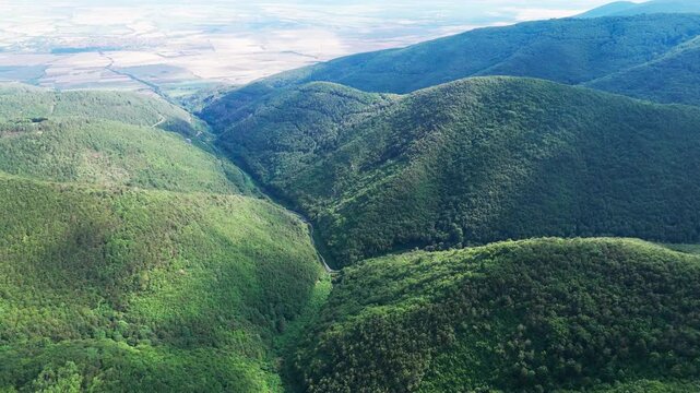 Drone follows the flow of a Balkan valley as dappled sunlight breaks through clouds, illuminating rolling green hills and distant open fields.