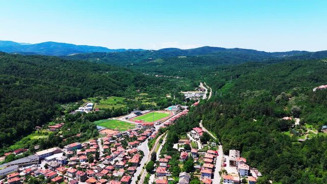 Drone push shot revealing Tryavna&rsquo;s valley landscape, residential areas, stadium, and surrounding hills defining the town&rsquo;s geography.