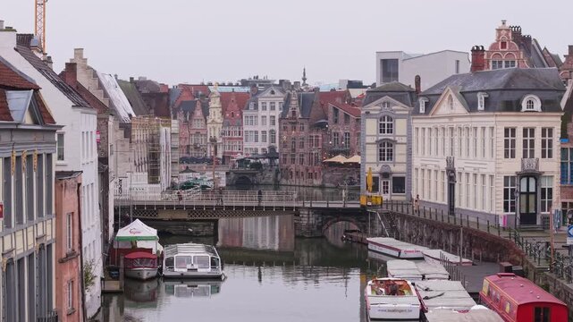 Drone pull-back movement over the Leie river, revealing the iconic medieval guild houses and picturesque waterfront of Graslei and Korenlei in Ghent, Belgium.
