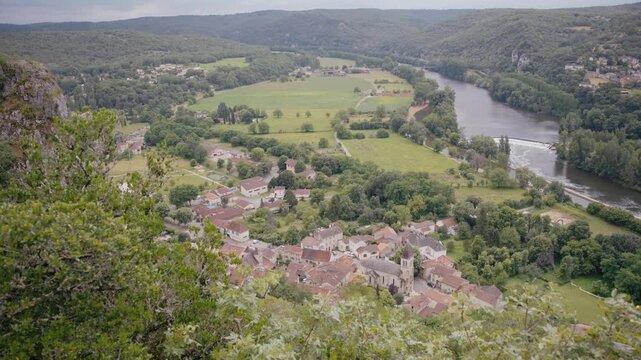Aerial panorama of Saint G&eacute;ry village in Lot valley. Historic French countryside architecture beside meandering river surrounded by green hills and cliffs.