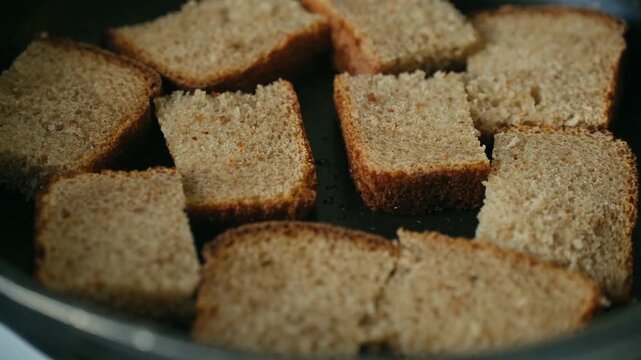 Slices of crusty brown bread toasting in a hot, non stick frying pan, making crispy homemade croutons for a salad or soup. A delicious and simple cooking process for a healthy meal