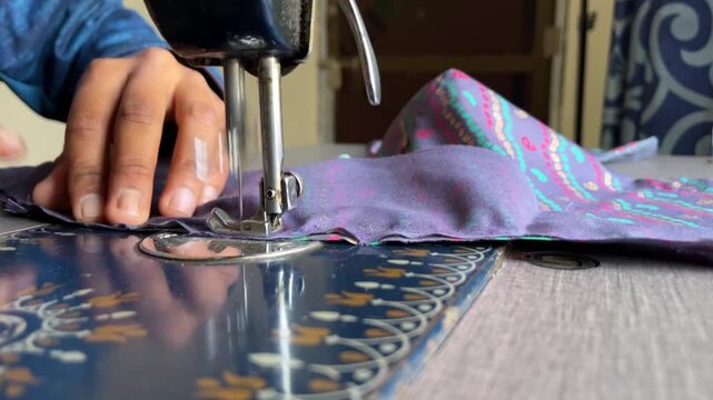 Close up of a tailor's hands using a vintage sewing machine to stitch colorful purple patterned fabric