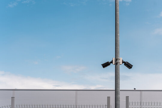 Two outdoor CCTV cameras on a pole near the fence