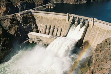 Fototapeta premium Massive hydroelectric dam releasing water through open spillway gates creating heavy mist