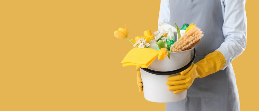 Female janitor with cleaning supplies and spring flowers on yellow background, closeup