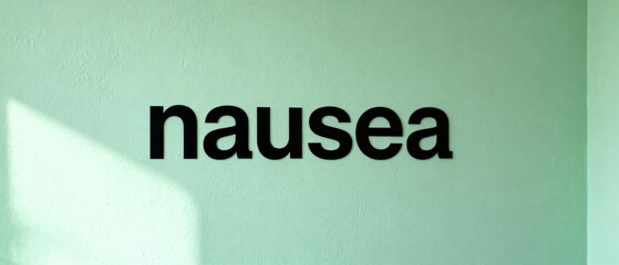 Conceptual image of the word nausea in black text on a minimalist pale green wall representing sickness.