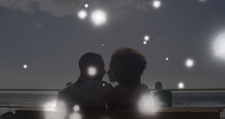 Obraz premium Image of glowing spots of light over african american couple embracing each other at the beach