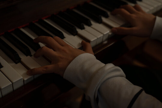 Close up of hands playing piano with moody lighting and artistic grain.
