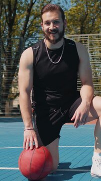 Portrait of tired athletic Lebanese man in sportswear after playing basketball game. Boy sitting relaxing on urban city court. Fitness routine on sports field. Motivation. Outdoors at sunny morning