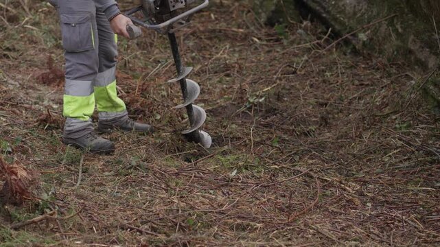 Person drilling soil hole with earth auger in forest ground