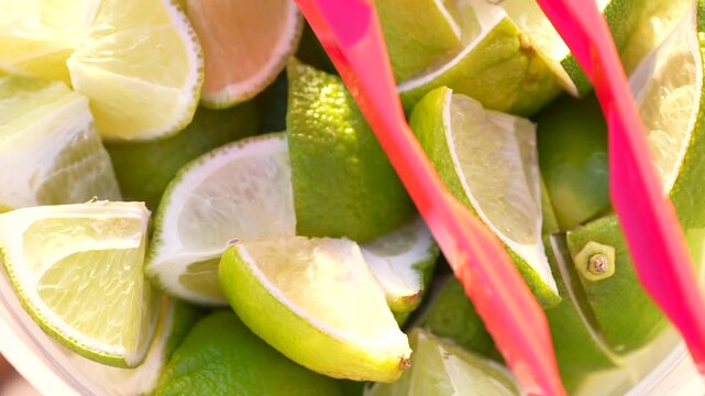 Overhead close-up of fresh lime wedges as condiments with a red tong at a street food taco stand, highlighting vibrant color, zest, and flavorful garnish.