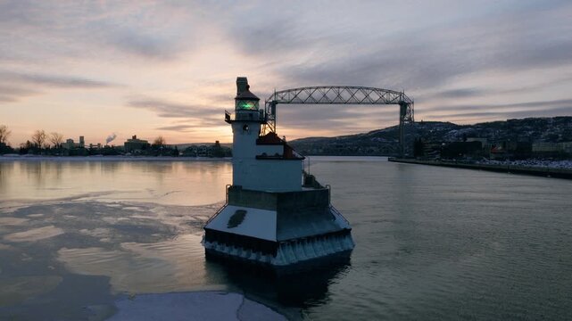 Cinematic drone reveal of the Duluth North Pier Lighthouse and Lift Bridge during a sub-zero winter sunrise with ethereal sea smoke on Lake Superior.