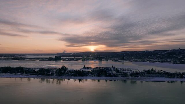 High-altitude aerial view of the Duluth Ship Canal, Park point neighborhoods, and harbor during a sub-zero sunset with dense sea smoke on Lake Superior.